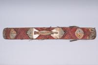 Shield  
plant fiber, feathers, beads  
159 × 21 x 12 cm  
Geographical classification: Papua New Guinea  
ZV 2000/708
Object description  
Shield with depiction of birds; red wickerwork wrapping of plant fiber; with feather and bead hanging; handle is embedded in shield.
Provenance  
Verein deutscher Seidenwebereien Krefeld (until unknown); J.F.G. Umlauff (until 1928); previous owner (unknown); transfer to Germany (unknown); appropriation in region of origin (unknown); manufacture (unknown).
Object history  
In July 1928, the "Verein der deutschen Seidenwebereien, Krefeld" (Association of German Silk Weavers, Krefeld) purchased a total of ten objects from various regions of the Pacific islands from the Hamburg-based company J.F.G. Umlauff, which specialized in the sale of ethnographic objects. The purchase was made in the wake of the exhibition "Color", which was on display at the Kaiser Wilhelm Museum from May 1 to 31, 1928.  
It is probably a battle shield of the inhabitants of the Vitu Islands. The wrapping of spliced red kelp, the carved bird and the painting reminiscent of faces are typical for them. Unlike the dance shields made on the islands, the handle is recessed into the board on the back.  
The battle shields could be the embodiment of a protective being, "symbolized by both the bird and human attributes" (Ingrid Heermann).